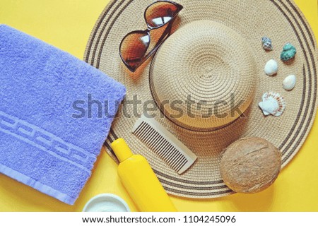 Purple towel, sun hat, sunglasses, yellow sunscreen bottle, wooden comb, coconut and seashells. Flat lay photo beach essentials. Summer holiday concept