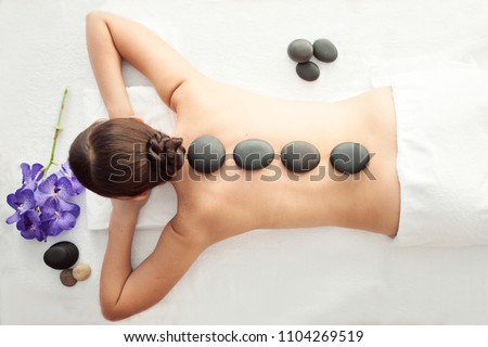 Stone treatment. Top view of beautiful young woman lying on front with spa stones on her back.  Beauty treatment concept. Royalty-Free Stock Photo #1104269519