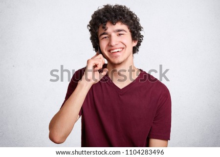 Happy teenager or hipster guy, speaks via cell phone with best friend, has delighted expression, recieves good news, smiles gently at camera, enjoys communication. People and modern technologies