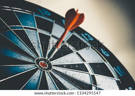 Close up shot of the dart arrow hit on bulleyes of dartboard to represent that the business reached the target of company with dark tone picture style. Target and goal as concept. Royalty-Free Stock Photo #1104295547