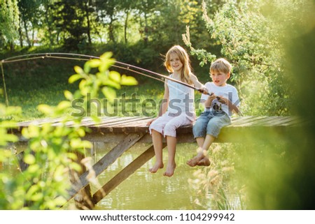 Barefoot boy and girl sitting on wooden pier with rod. Love, friendship concept. Beautiful romantic sunset picture.