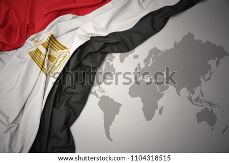 waving colorful national flag of egypt on a gray world map background.