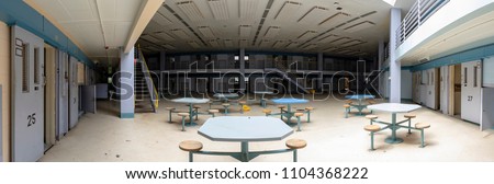 Common area inside abandoned prison cellblocks with open doors. Royalty-Free Stock Photo #1104368222