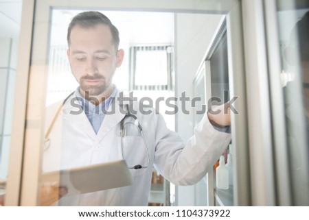 Modern doctor with tablet searching in the net while looking for information about new medicine