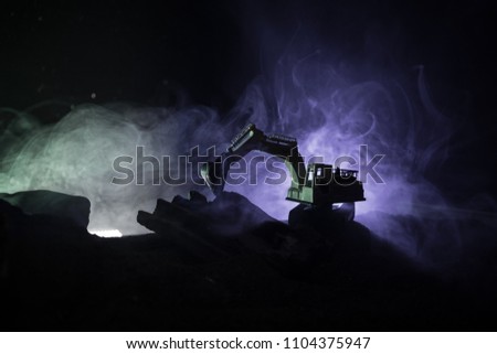 Construction site on a city street. A yellow digger excavator parked during the night on a construction site. Industrial concept table decoration on dark foggy toned background. Selective focus