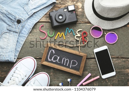 Inscription Summer Camp with smartphone, sunglasses and clothes on wooden table