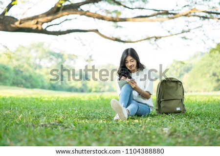 Portrait brunette young Asian casual hipster girl relaxing outdoors while writing in her diary beautiful park .