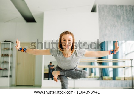 Close-up of charming young woman in a black suit doing sophisticated yoga exercise stand on one leg with hands apart on white isolated background