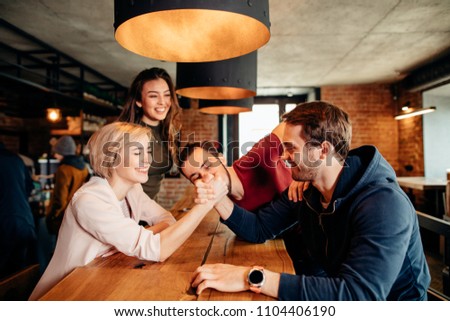 Young attractive women girl friends and their new male friends playing, wrestling and smiling while spending time together at trendy pub. Fun, holiday, youth and togetherness Concept .