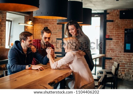 Cheerful group of students friends couple having fun arm wrestling each other in fashionable pub.