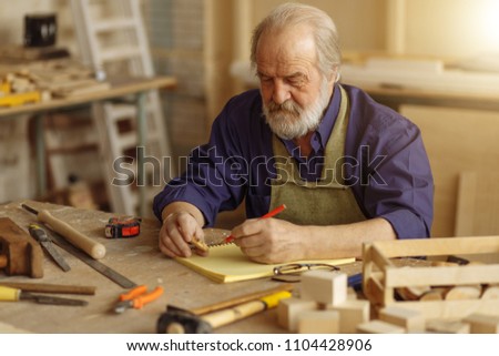 old artisan in working outfit writing designing ideas in the factory. close up photo