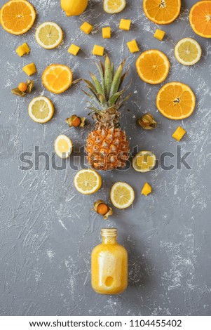 Sweet yellow smoothie with pineapple, citrus and yellow fruits on gray wooden table, top view.