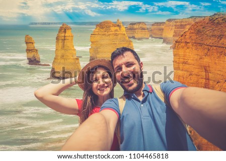 handsome couple backpackers take selfie in front of the cliff of twelve apostles on the ocean of Victoria region in a summer day, Victoria, Australia.