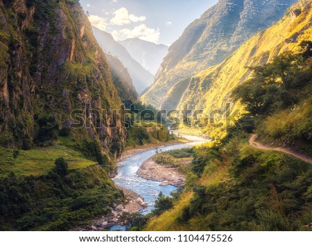 Colorful landscape with high Himalayan mountains, beautiful curving river, green forest, blue sky with clouds and yellow sunlight at sunset in summer in Nepal. Mountain valley. Travel in Himalayas Royalty-Free Stock Photo #1104475526