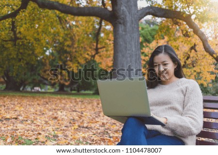 Asian beautiful smiling woman working with laptop while sitting in garden with green grass and falling leaf in autumn.Concept of people using technology.
