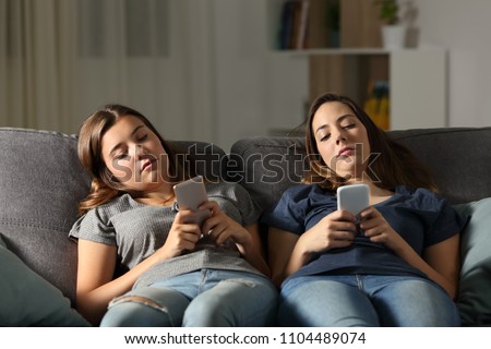 Bored friends using their smart phones sitting on a couch in the living room at home
