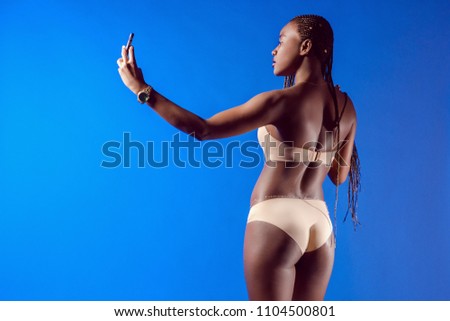The African model takes pictures of herself. Girl with African pigtails. Black photo model. A black girl is taking pictures of herself on the phone.