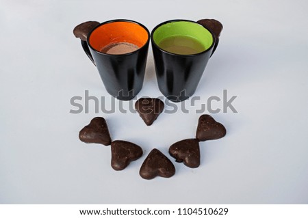 Two colorful mugs and chocolate hearts closeup