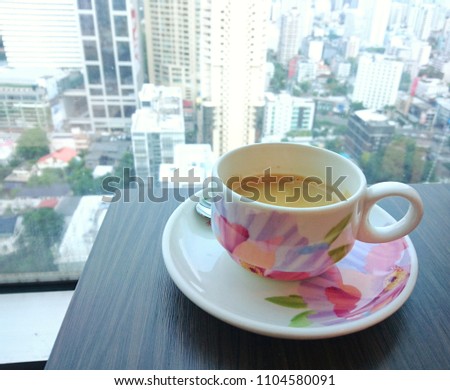 The morning coffee on the table near the window glass, background is city scape view and sky scrapper,