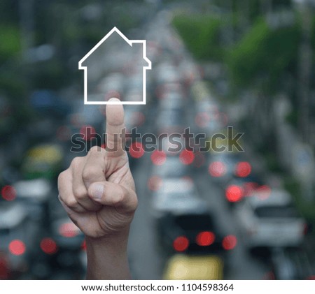Hand pressing house icon with copy space over blur of rush hour with cars and road, Real estate concept