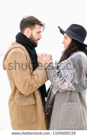 Portrait of young man with beard holding woman hand in white background, wearing coat with scarf. Concept of couple seasonal winter photo session and romantic feelings.