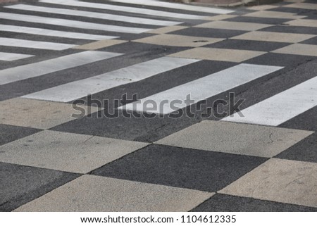 Outdoor view of traffic signs drawn on an asphalt road in a french city. Pattern of white and grey bands and squares. Abstract design with geometric and graphic shapes. Sidewalk with zebra crossing.