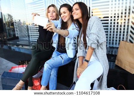 Three women taking a selfie while shopping in a clothing store. They are happy and smiling at camera. Shopping concept