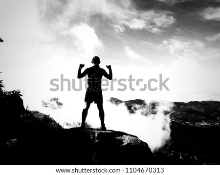 Silhouette of male athlete standing on the deep cliff and cloud.