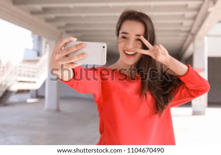 Attractive young woman taking selfie with phone outdoors
