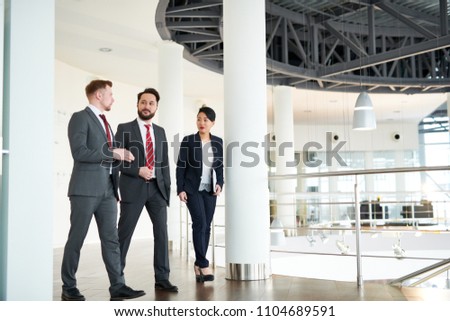 Multi-ethnic group of white collar workers chatting animatedly with each other while walking along spacious office lobby