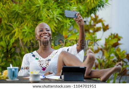 young happy and attractive black afro American woman working with digital tablet outdoors at cafe taking selfie picture with mobile phone relaxed and cheerful in digital nomad success
