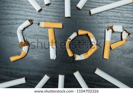 Top view of cigarette butts shaping word of stop with cigarettes above the table. Concept for quitting smoking 