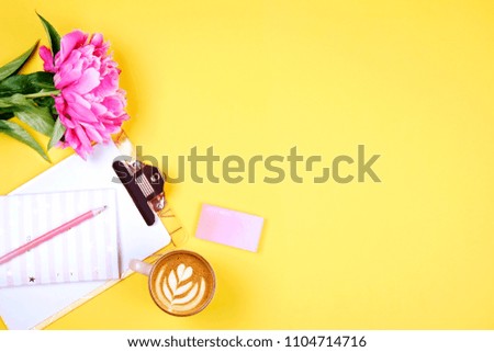 Woman's workplace, blank paper sheet on a clipboard, cup of coffee, pink pen & lilac peony flowers on yellow table top background. Feminine flat lay composition w/ purple bouquet. Close up, copy space