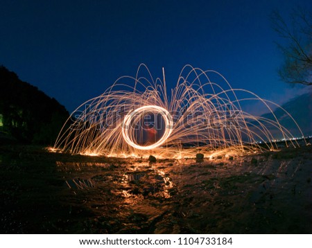 light lines of steel wool with long exposure, speed motion abstract background in the twilight blue sky silhouette branch tree and mountain.