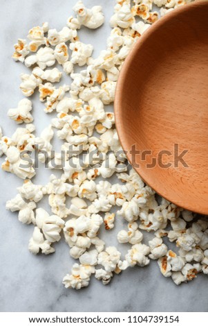 Salted popcorn and an empty deep bowl on a marble background.