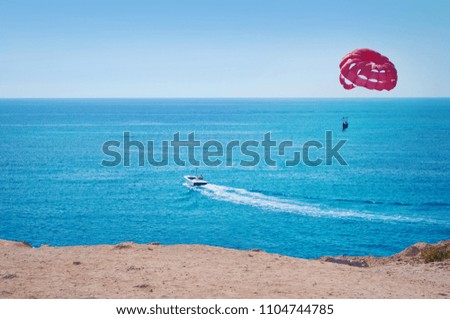 Vibrant image of two people parasailing on a red parachute bulled by one boat on the background of blue sea water and cloudless sky. Concept of extreme sports, adventure and fun. Cyprus, summer