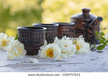 Ceramic cups , teapot and white dog roses on a old wooden table in garden. Aromatic and invigorating tea with wild rose.