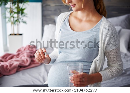 Young pregnant woman taking capsule  Royalty-Free Stock Photo #1104762299