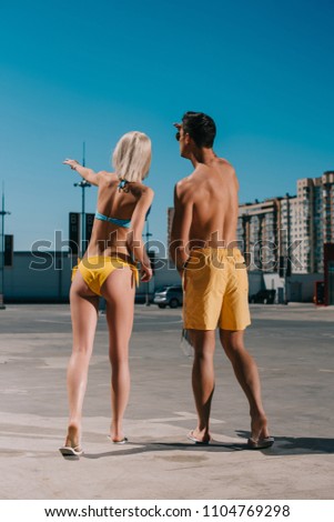 rear view of young couple in bikini and swimming shorts pointing somewhere on parking