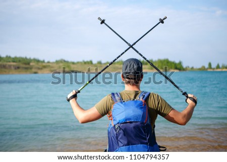 Image from back of tourist man with crossed walking sticks on hill