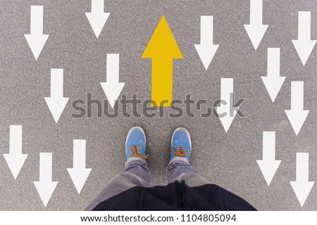 Opposing direction arrows on asphalt ground, feet and shoes on floor, personal perspective footsie concept for finding your own way Royalty-Free Stock Photo #1104805094