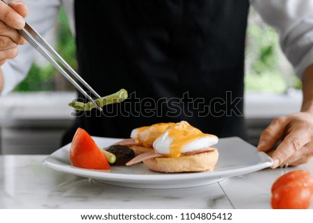 Concept picture, chef is preparing breakfast in hotel by put asparagus on egg benedict