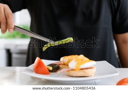 Concept picture, chef is preparing breakfast in hotel by put asparagus on egg benedict