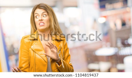 Beautiful young woman disgusted and angry, keeping hands in stop gesture, as a defense, shouting at restaurant
