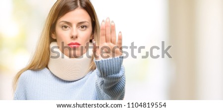 Young injured woman wearing neck brace collar annoyed with bad attitude making stop sign with hand, saying no, expressing security, defense or restriction, maybe pushing