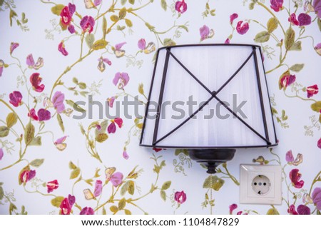 A small sconce above the bed on a background of floral wallpaper