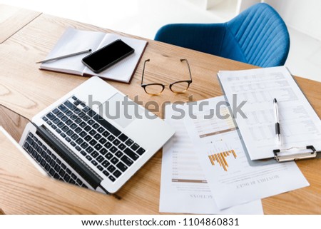 Top view of office things lying on wooden table. Laptop, clipboard, glasses, pencil, notebook. Workplace with nobody