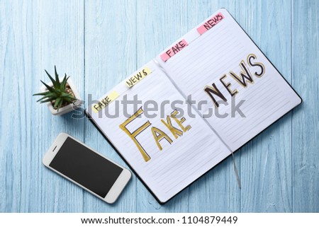 Notebook with words FAKE NEWS and mobile phone on wooden background