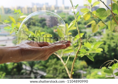 The man's hand hold bubble. Green leaves.