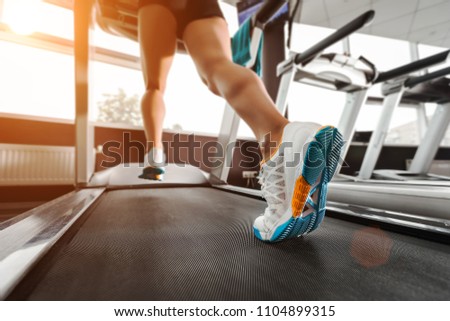 close up womans feet running on the treadmill at the gym over sunrise. wearing in white orange blue sneakers. Cardio exercise Royalty-Free Stock Photo #1104899315